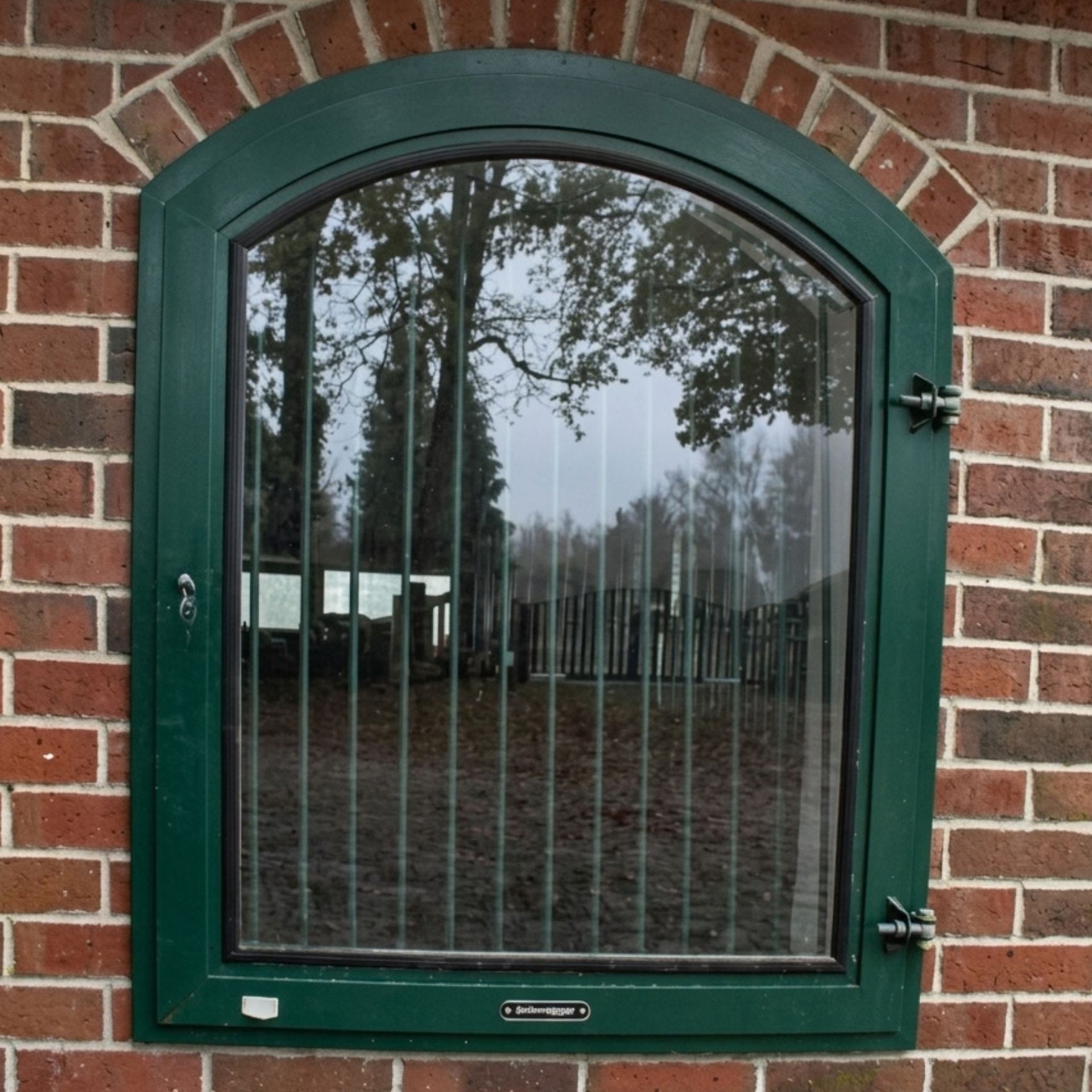 bogenförmiges Fenster, grüner Rahmen, Backsteinwand, Doppelverglasung, reflektierende Gitter