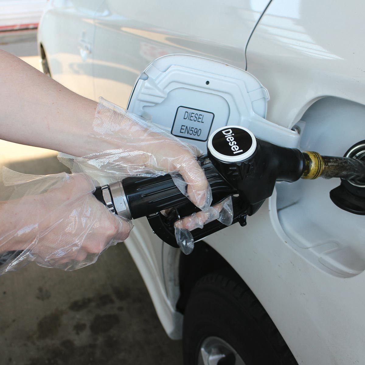 Mano con guanto di plastica che tiene la pistola del gasolio sull'auto bianca