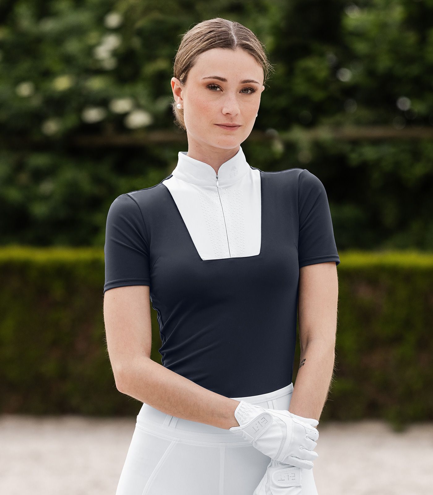 Femme en maillot d'équitation sombre à col blanc et gants d'équitation blancs