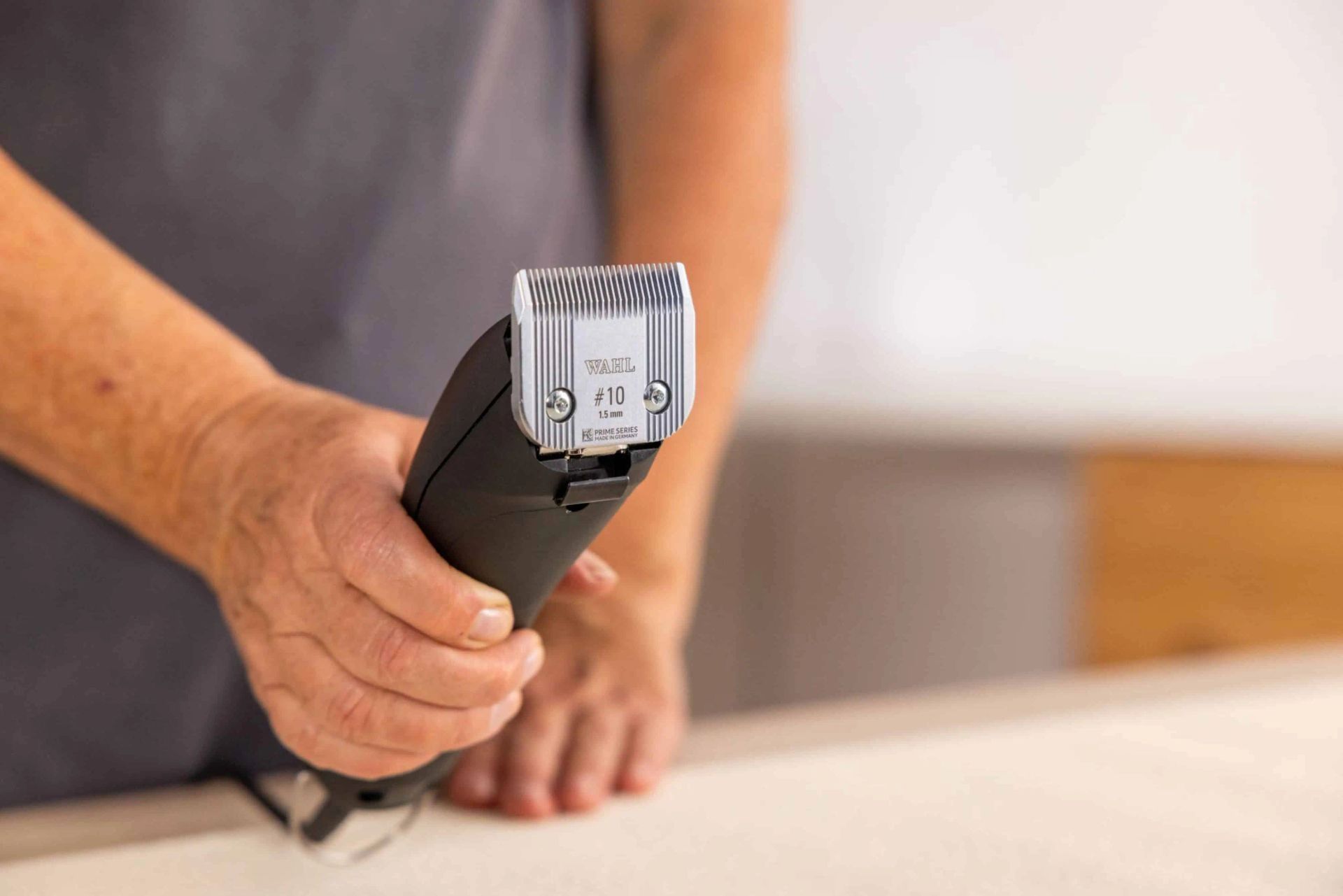 Person haelt eine Schermaschine mit Scherkopf in der Hand ueber einem Tisch
