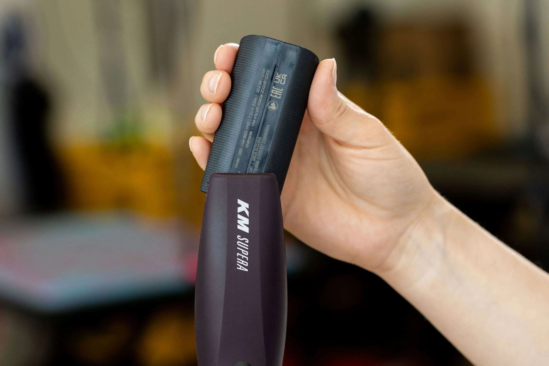 Hand haelt Akku einer Schermaschine mit Aufdruck KM Supera