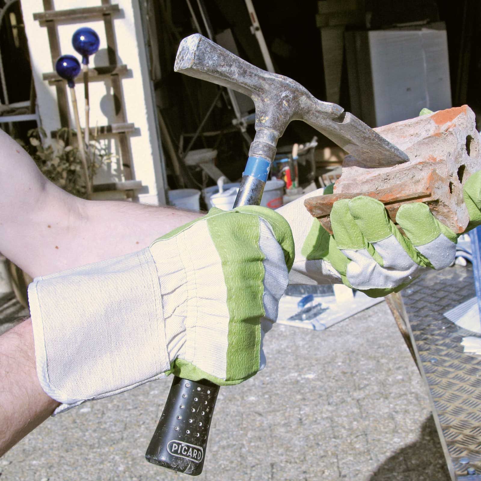 Braccio con guanto da lavoro grigio-verde con martello e mattoni