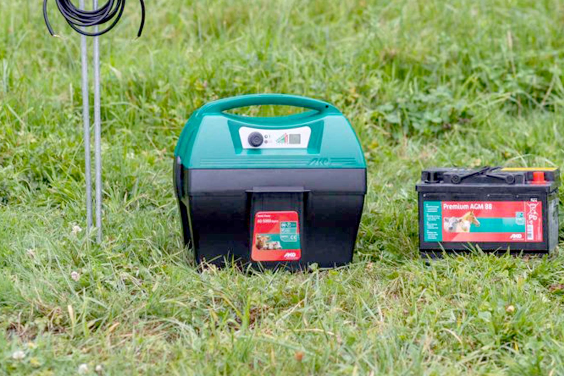 Grünes Weidezaungerät mit Batterie und Erdungsstab auf Wiese