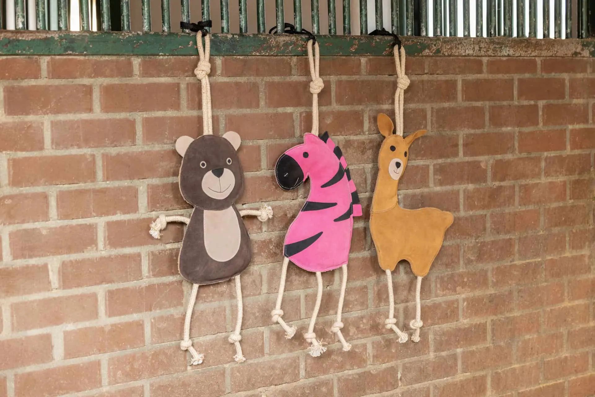 Trois jouets en forme d'animaux suspendus à des cordes, ours, zèbre et lama, devant un mur de briques