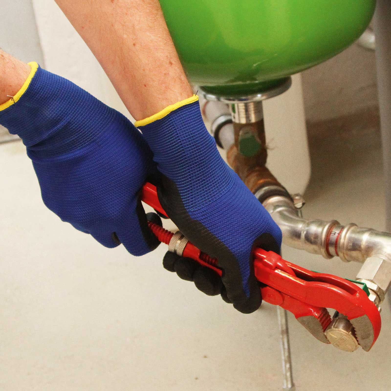 Mani con guanti da lavoro blu usano una chiave per tubi rossa su una tubatura
