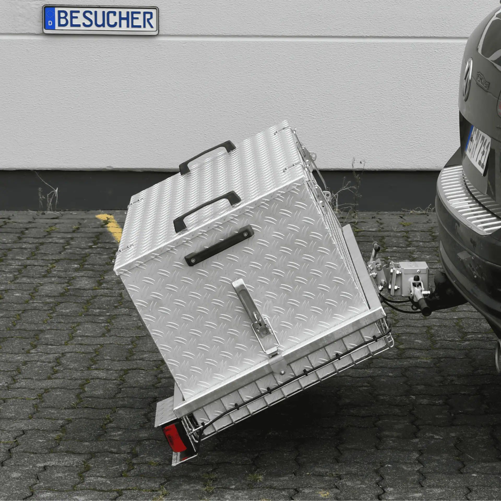 Silberfarbene Aluminiumbox mit Riffelblechmuster an einer Anhängerkupplung eines Autos