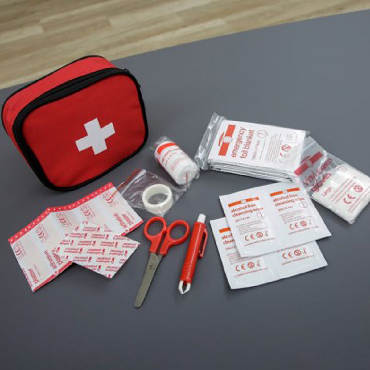 Rote Erste Hilfe Tasche mit weißem Kreuz, daneben ausgebreitetes Verbandsmaterial und Schere
