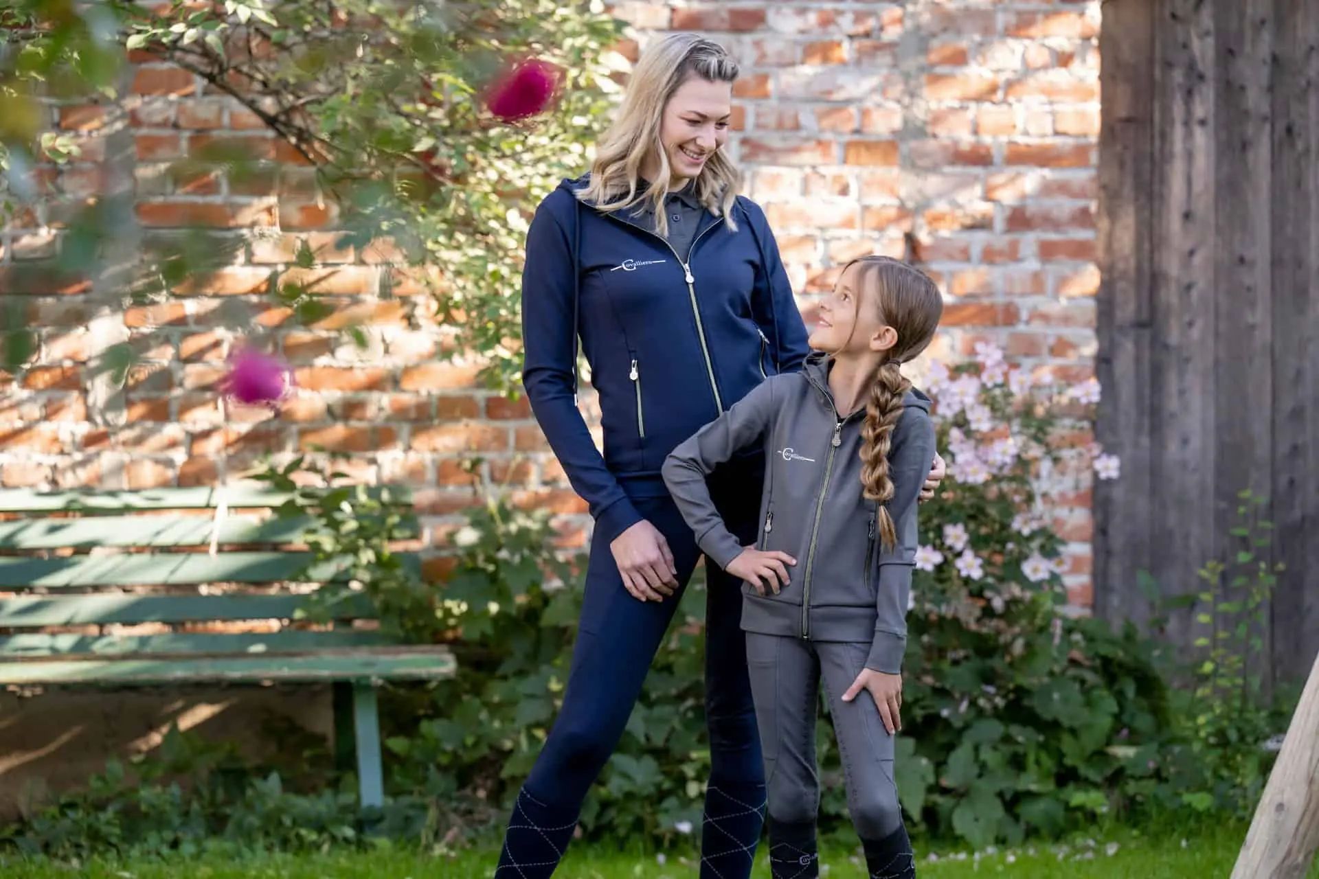 Woman and girl in dark riding gear standing laughing in the garden