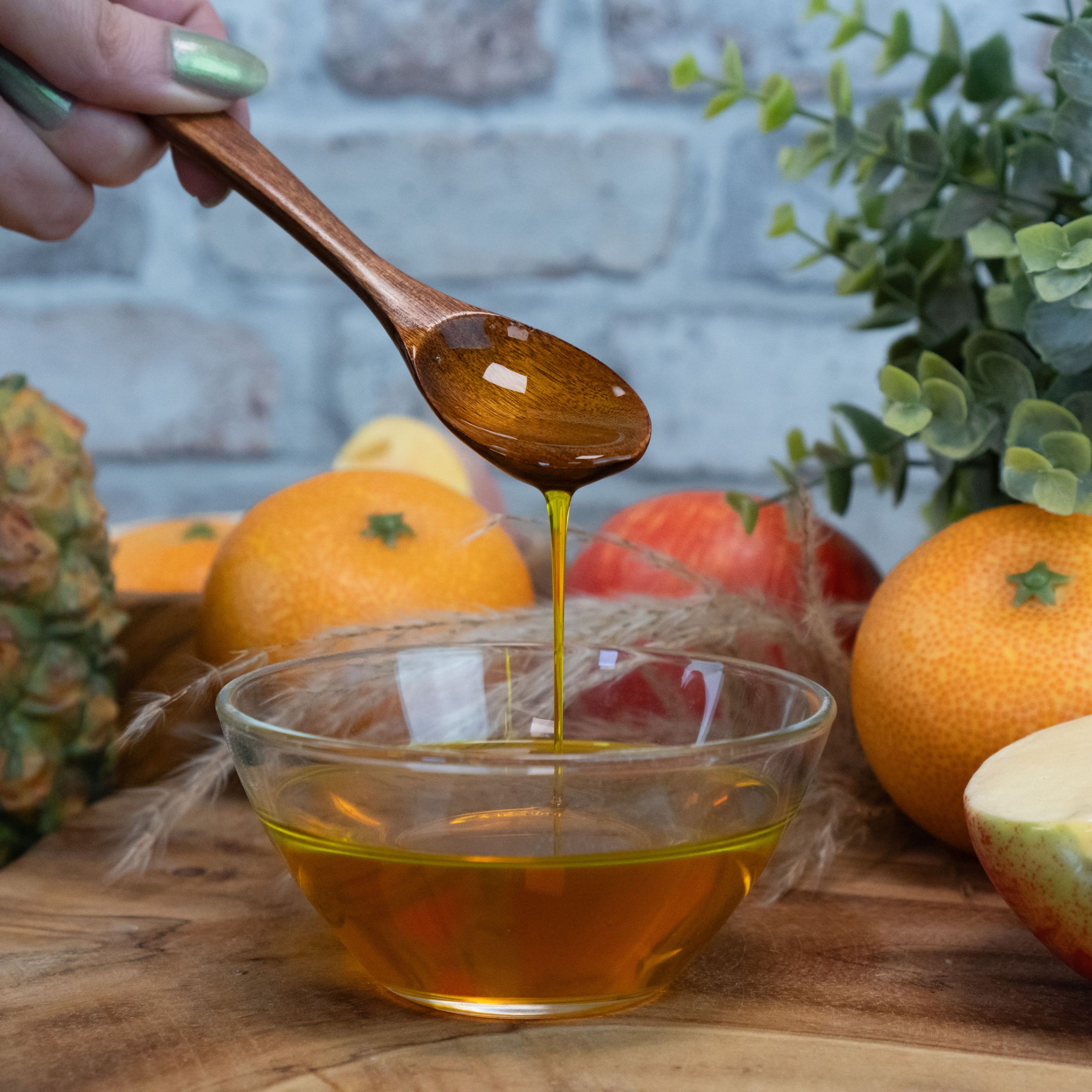 Honig, goldene Flüssigkeit, Holzlöffel, Schale mit Flüssigkeit, Frucht im Hintergrund